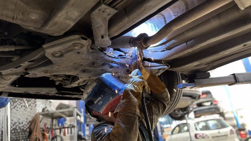 Сварка гофры выхлопной системы снизу автомобиля на подъёмнике, вспышка дуги и искры
